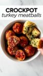 crockpot meatballs in a white bowl with a hand grabbing garlic bread with overlay text "crockpot turkey meatballs".