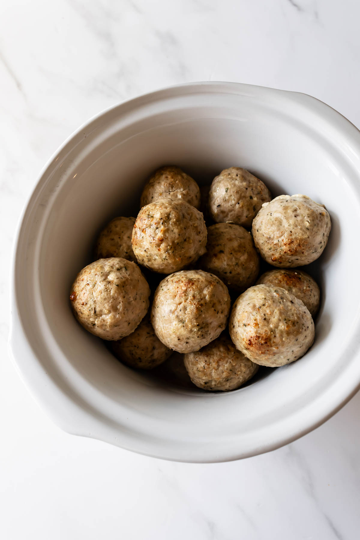 turkey meatballs in a white slow cooker on a white table.