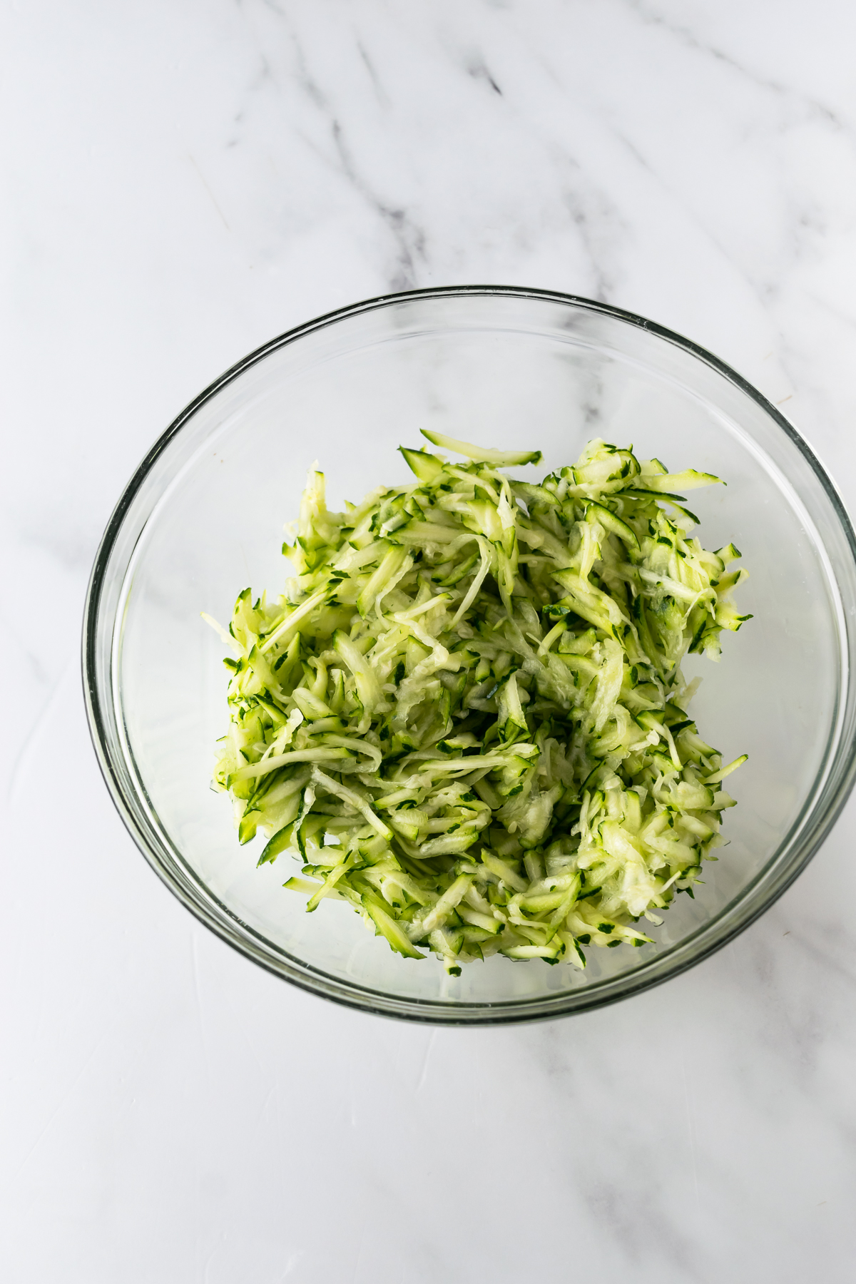 shredded zucchini in a bowl on a white table.