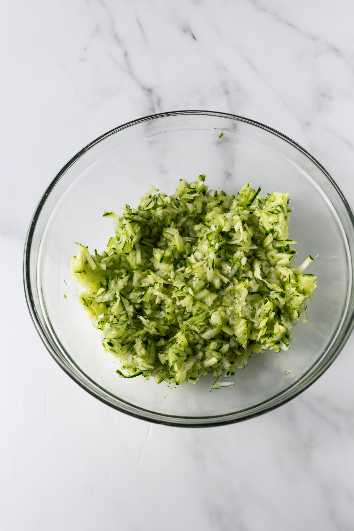 chopped shredded zucchini in a bowl on a white table.