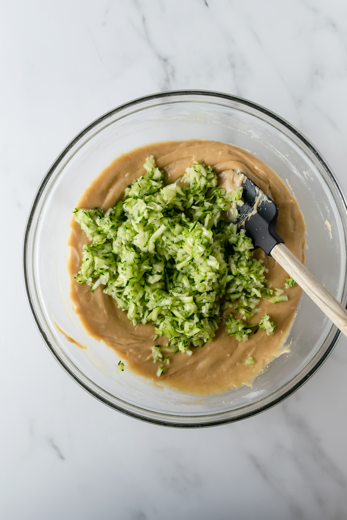 zucchini bread batter with shredded zucchini and a rubber spatula.