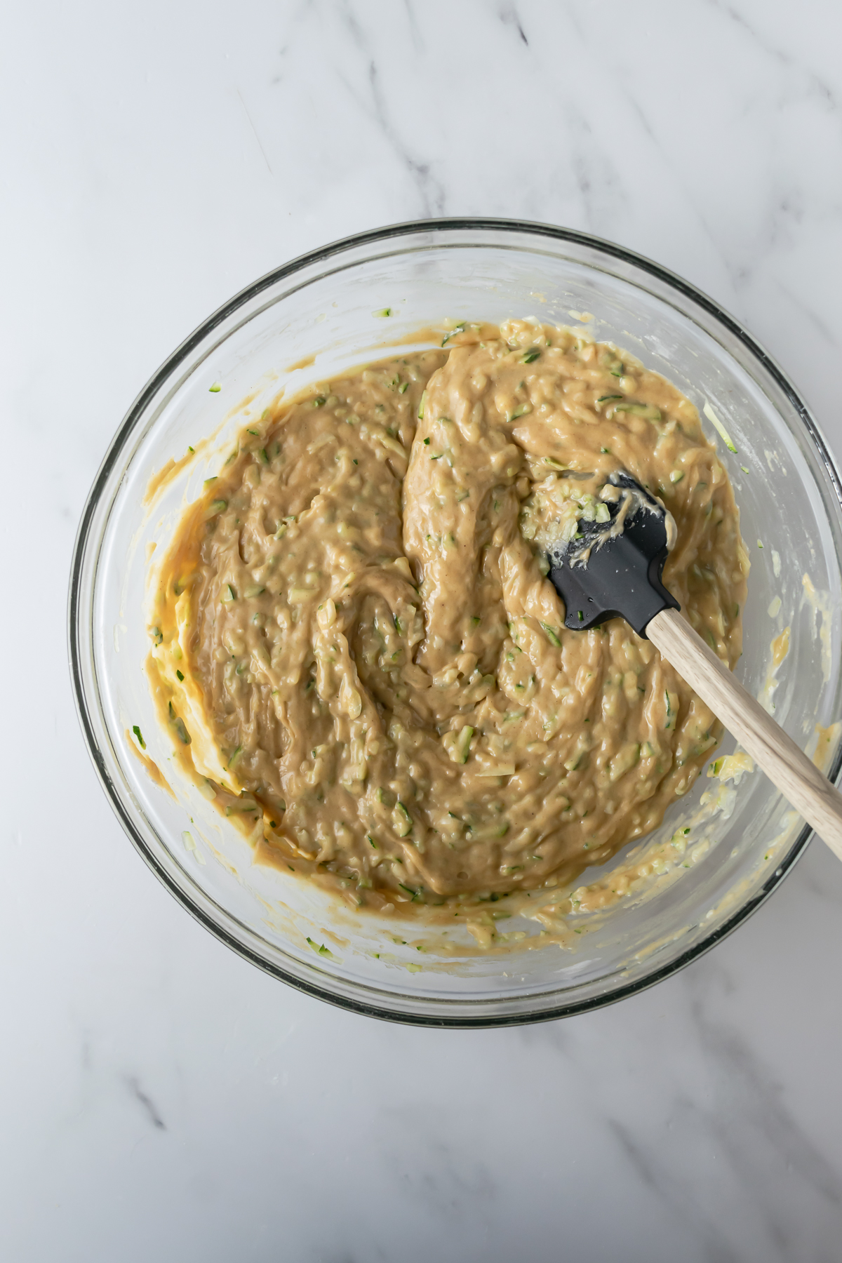 zucchini bread batter in a bowl on a white table with a spatula.