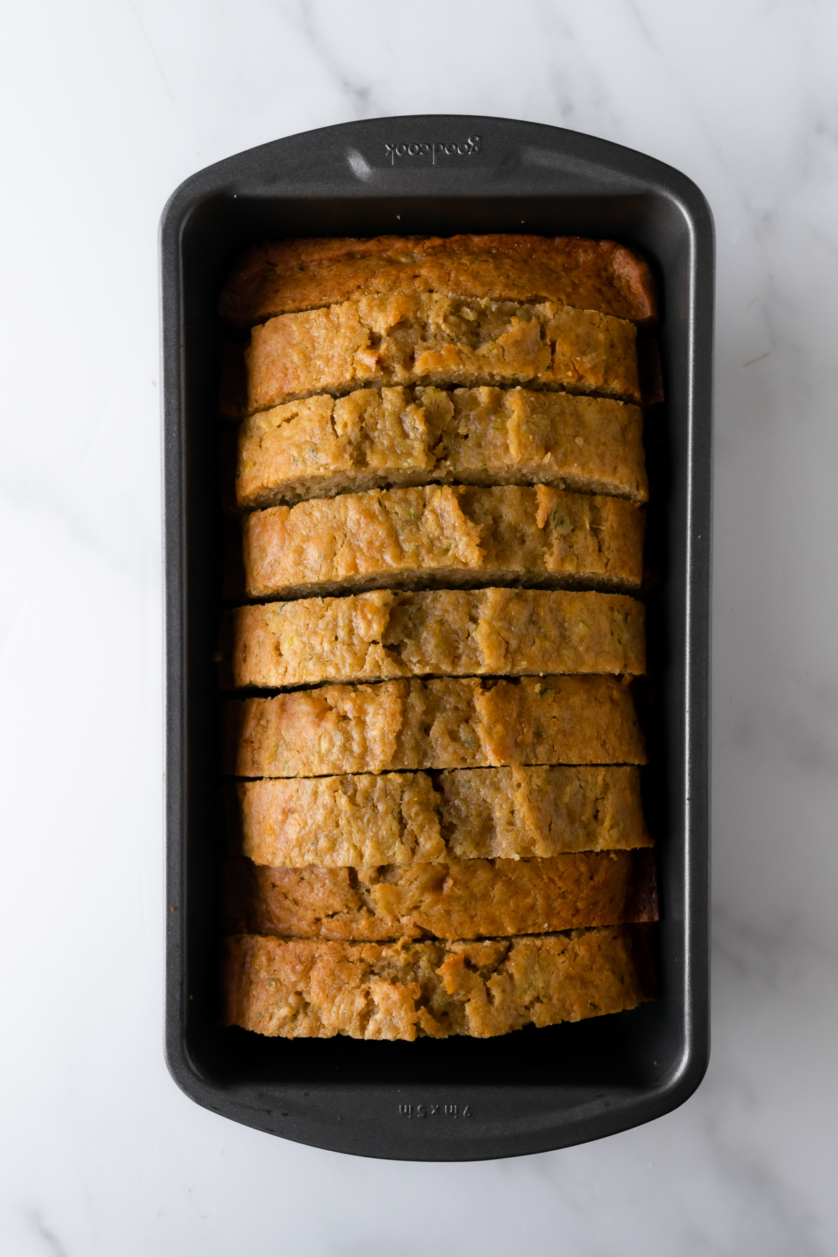 zucchini bread cut into slices in a loaf pan on a white table.