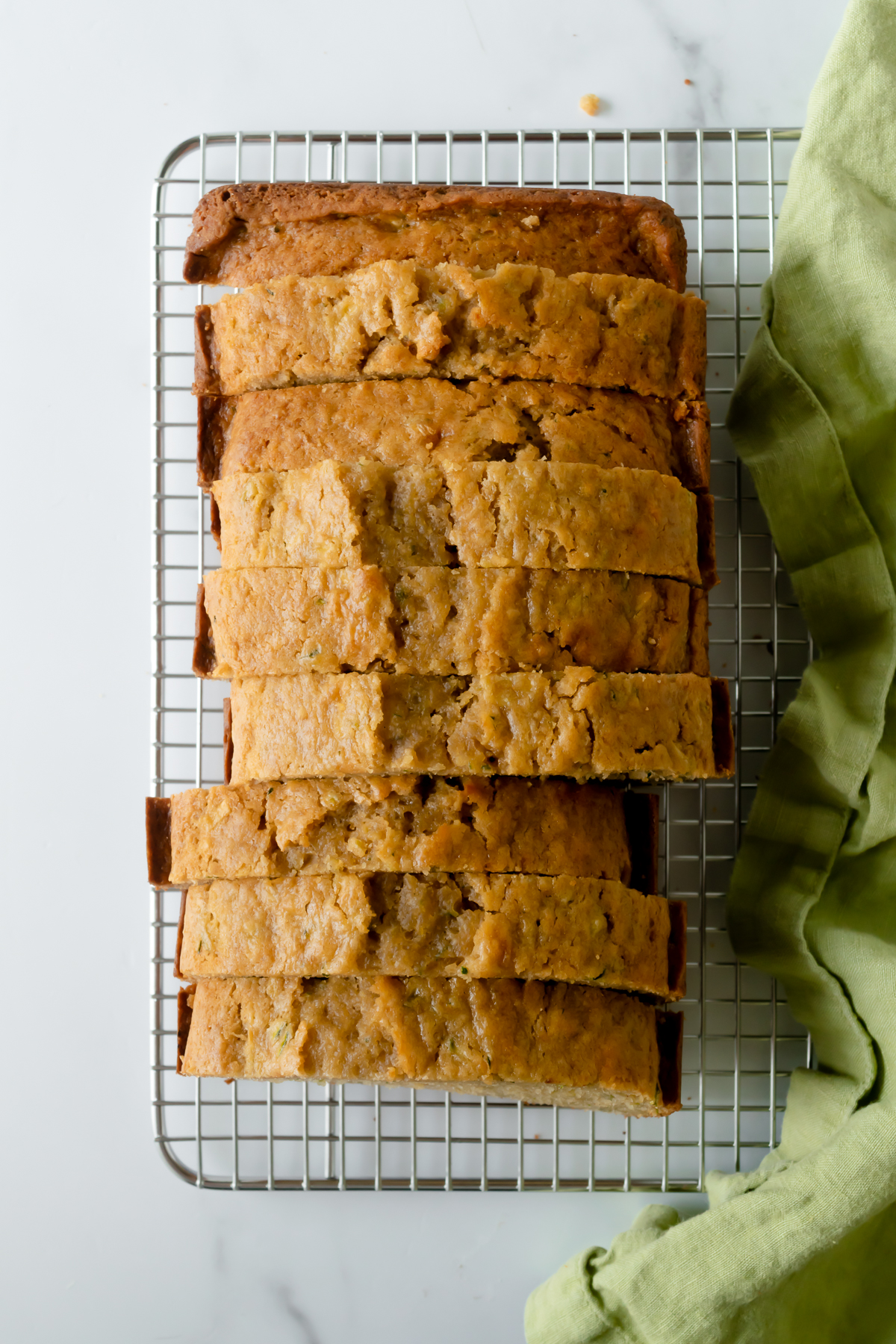 zucchini bread cut into slices on a metal cooling rack with a green napkin.