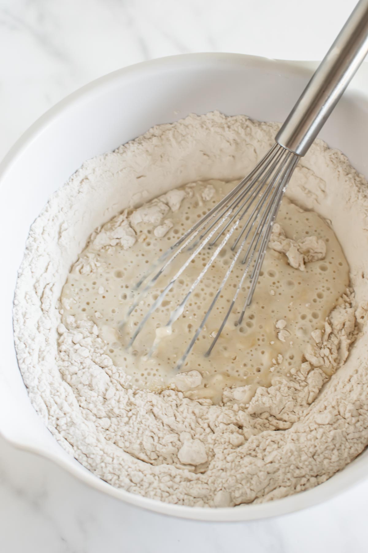 flour with wet ingredients in a white bowl with stainless steel whisk for pancake batter.