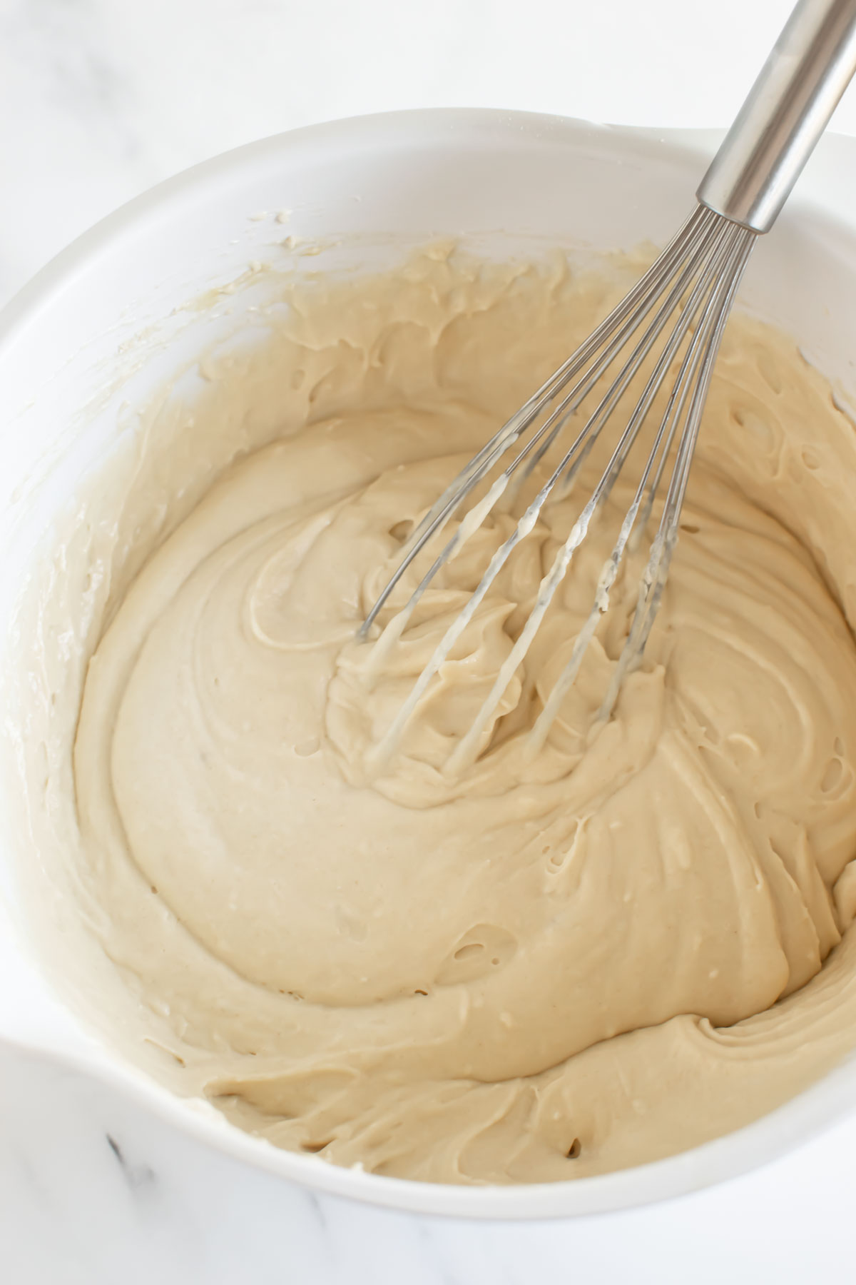 pancake batter in a white bowl with a stainless steel whisk.