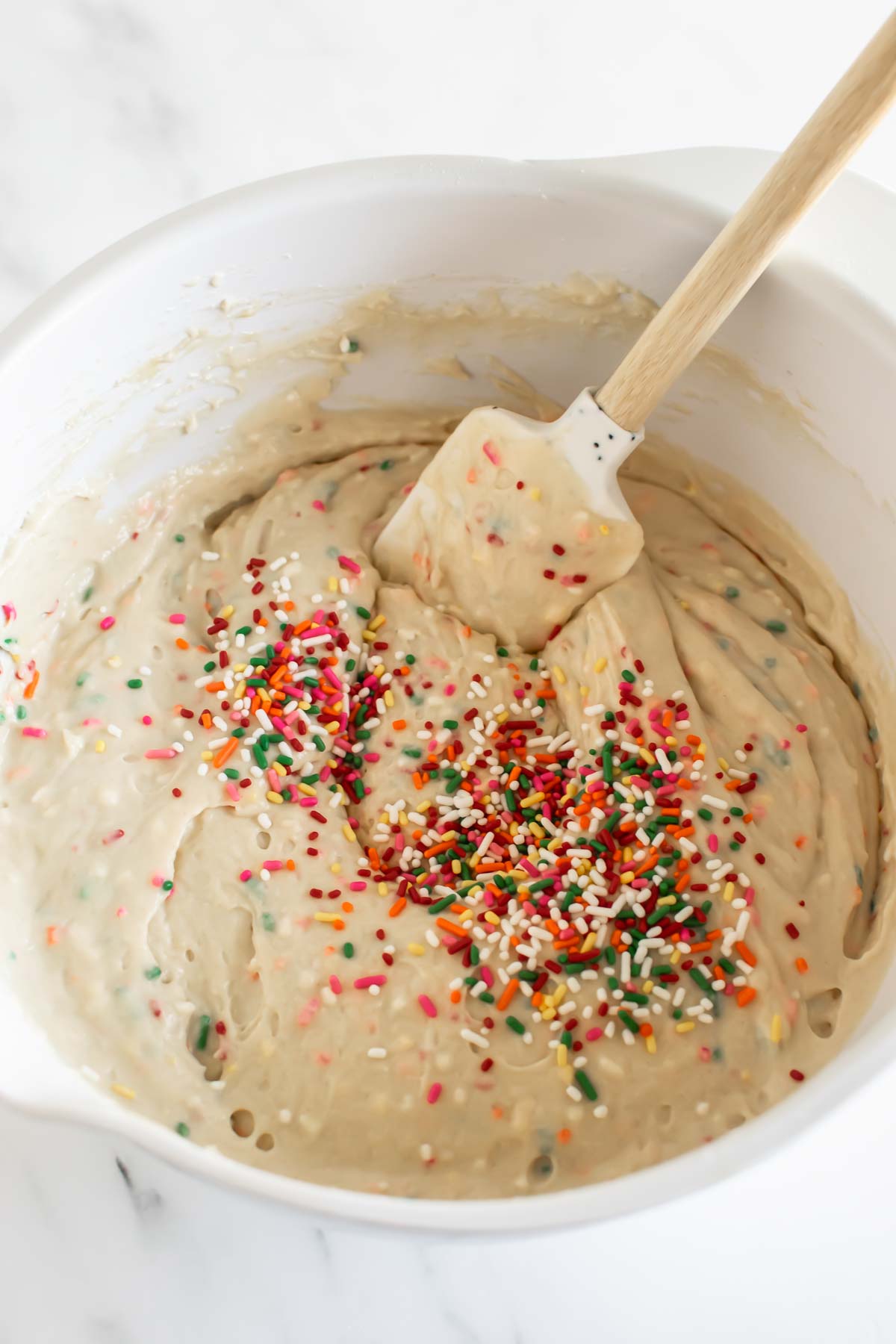 pancake batter with sprinkles in a white bowl with a spatula.