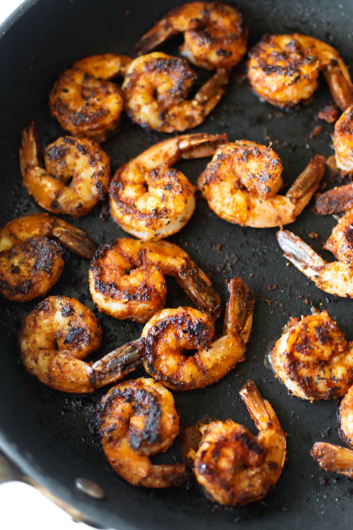 cooked blackened shrimp in a black pan.