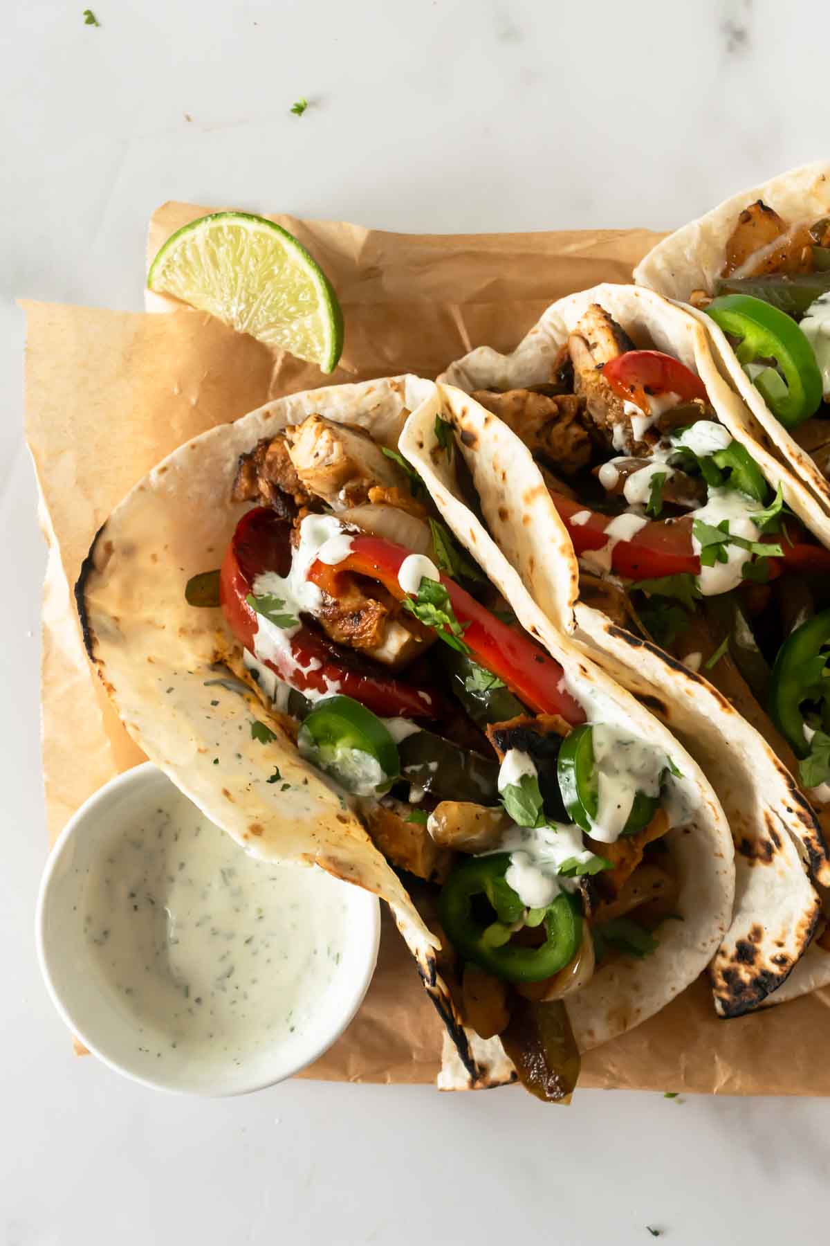 3 chicken fajitas sitting on parchment paper with sour cream.