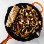 chicken fajitas in a black and orange skillet with tortillas rolled in parchment paper.