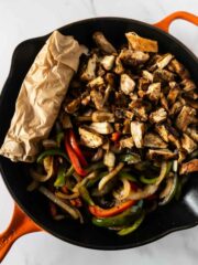 chicken fajitas in a black and orange skillet with tortillas rolled in parchment paper.