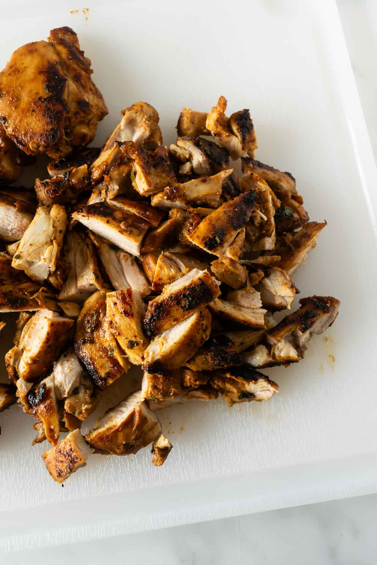 cooked sliced chicken thighs with fajita seasoning on a white cutting board.