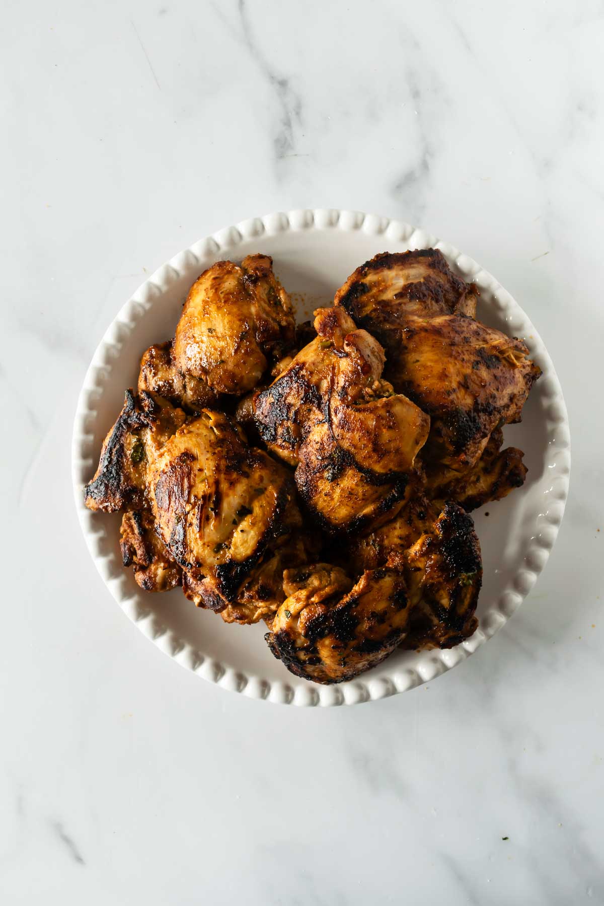 cooked charred fajita chicken thighs on a white round plate.