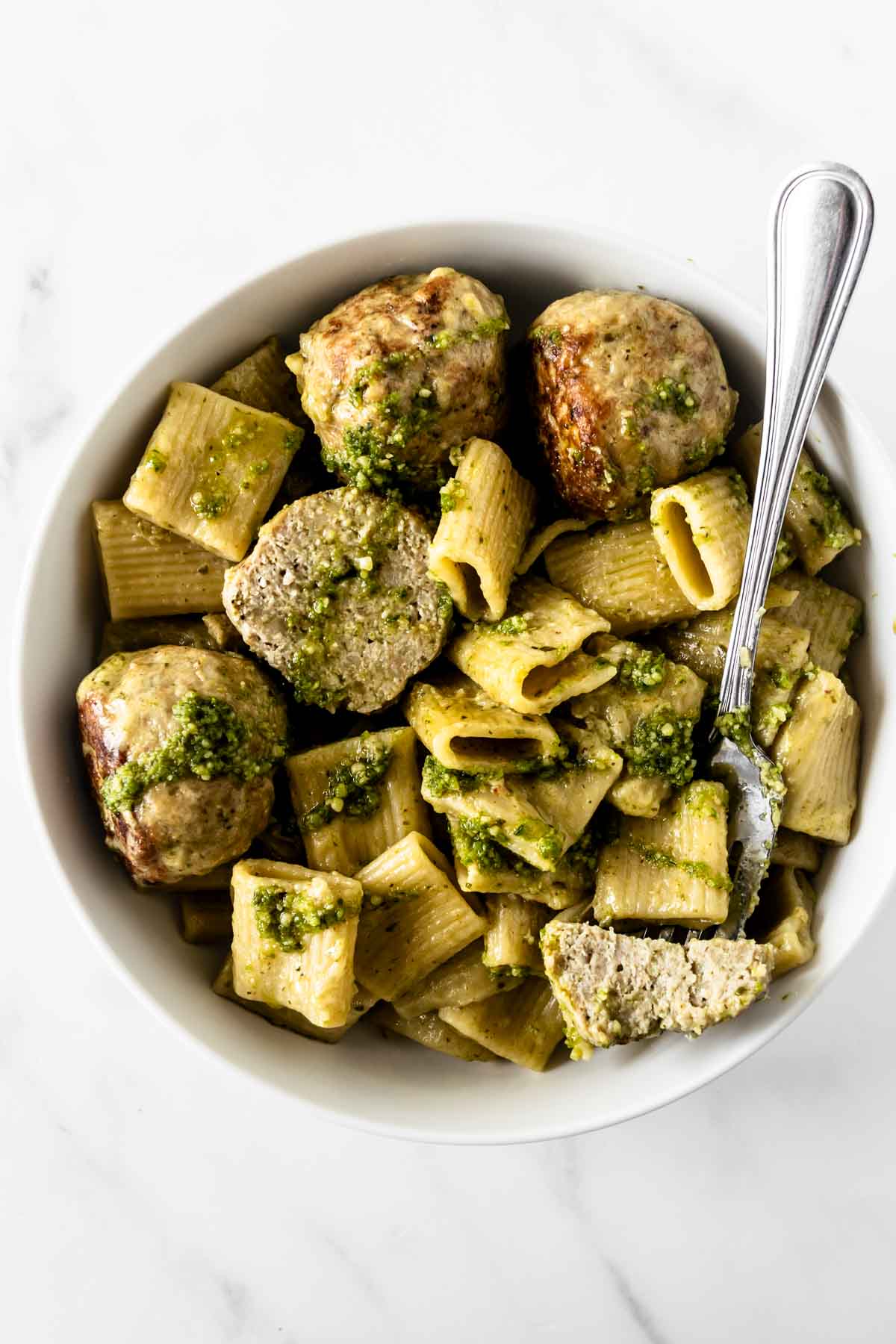 pesto chicken meatballs with pasta topped with pesto in a white bowl with a fork.