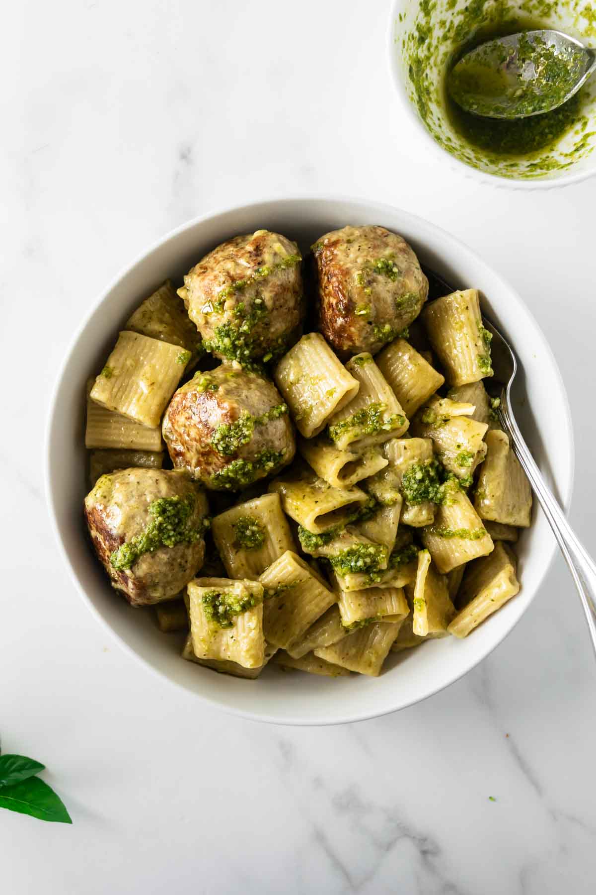 chicken pesto meatballs with rigatoni pasta topped with basil pesto in a white bowl.