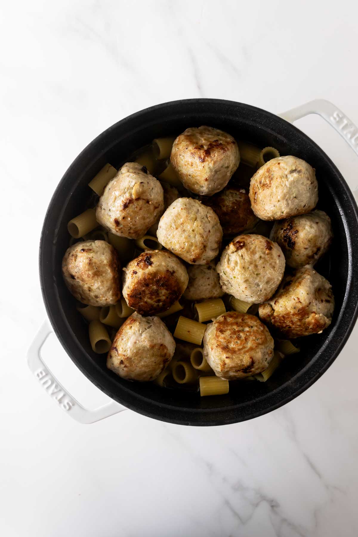 chicken meatballs and pasta in a black pot.