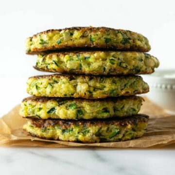 stacked zucchini fritters sitting on parchment paper.