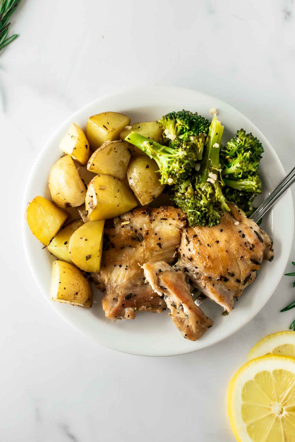 garlic lemon rosemary chicken with potatoes and broccoli on a white plate.