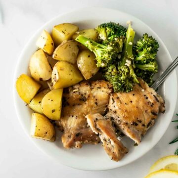 baked lemon rosemary chicken and potatoes with broccoli on a white plate.