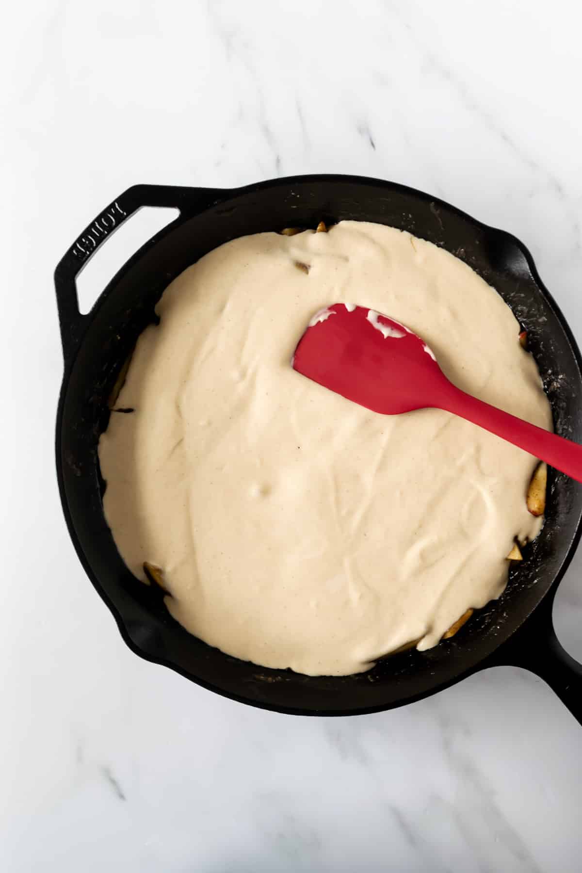 spreading pancake batter over cinnamon apples in a skillet.