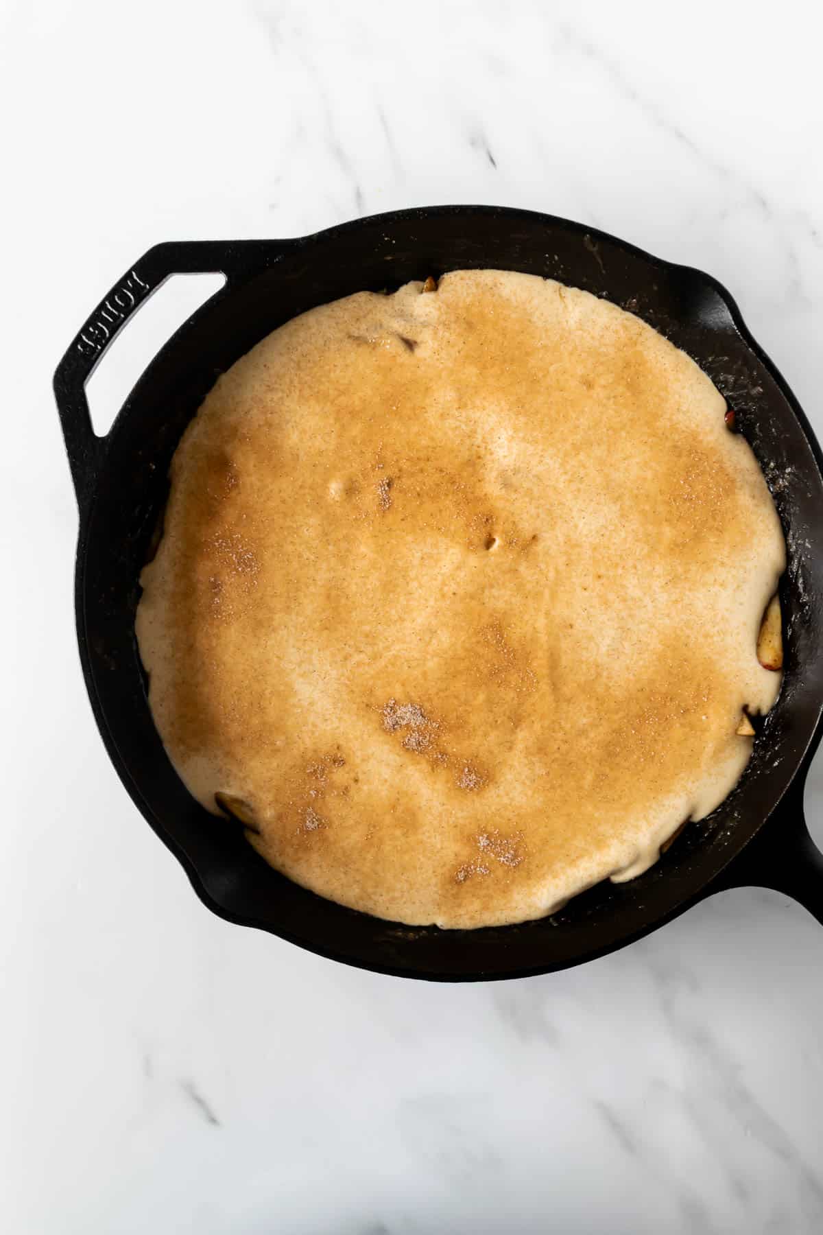 pancake batter over cinnamon apples topped with cinnamon sugar in a skillet.