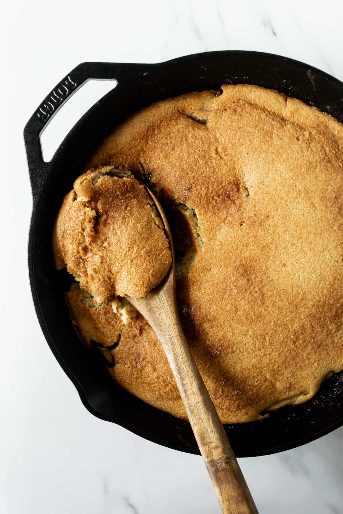 a scoop of cinnamon and apple pancakes on a wooden spoon in a skillet.