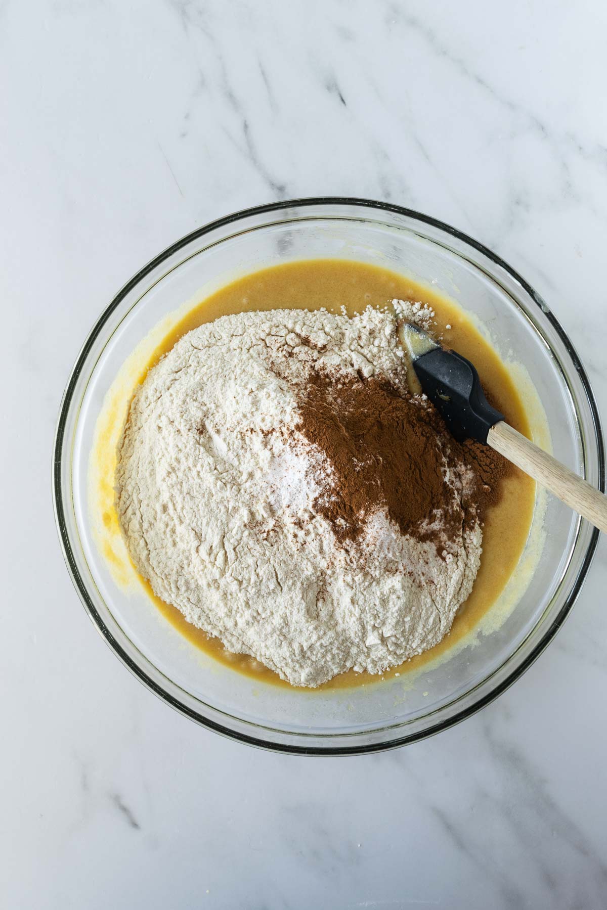 flour and cinnamon on wet ingredients in a clear bowl.