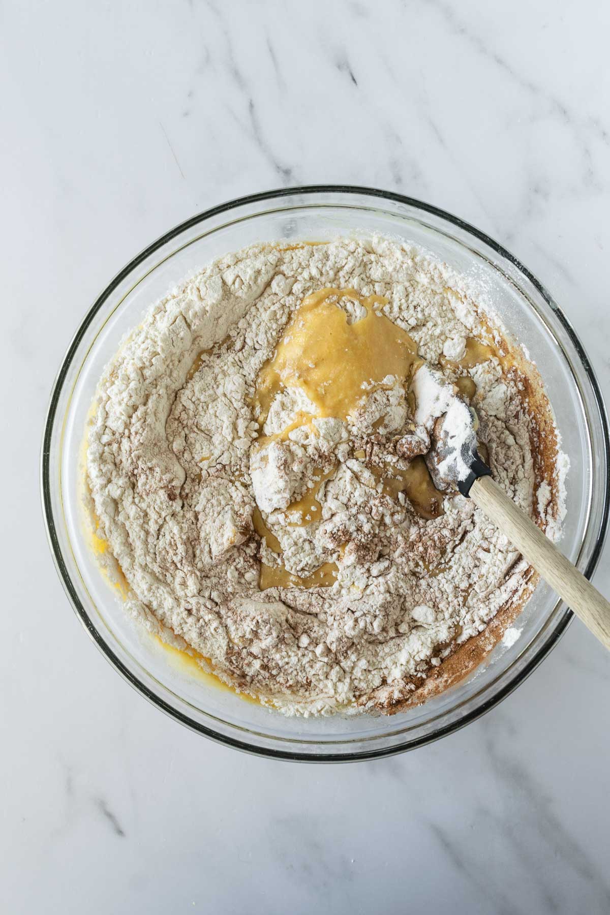 apple cake batter with a spatula in a glass bowl on a white table.