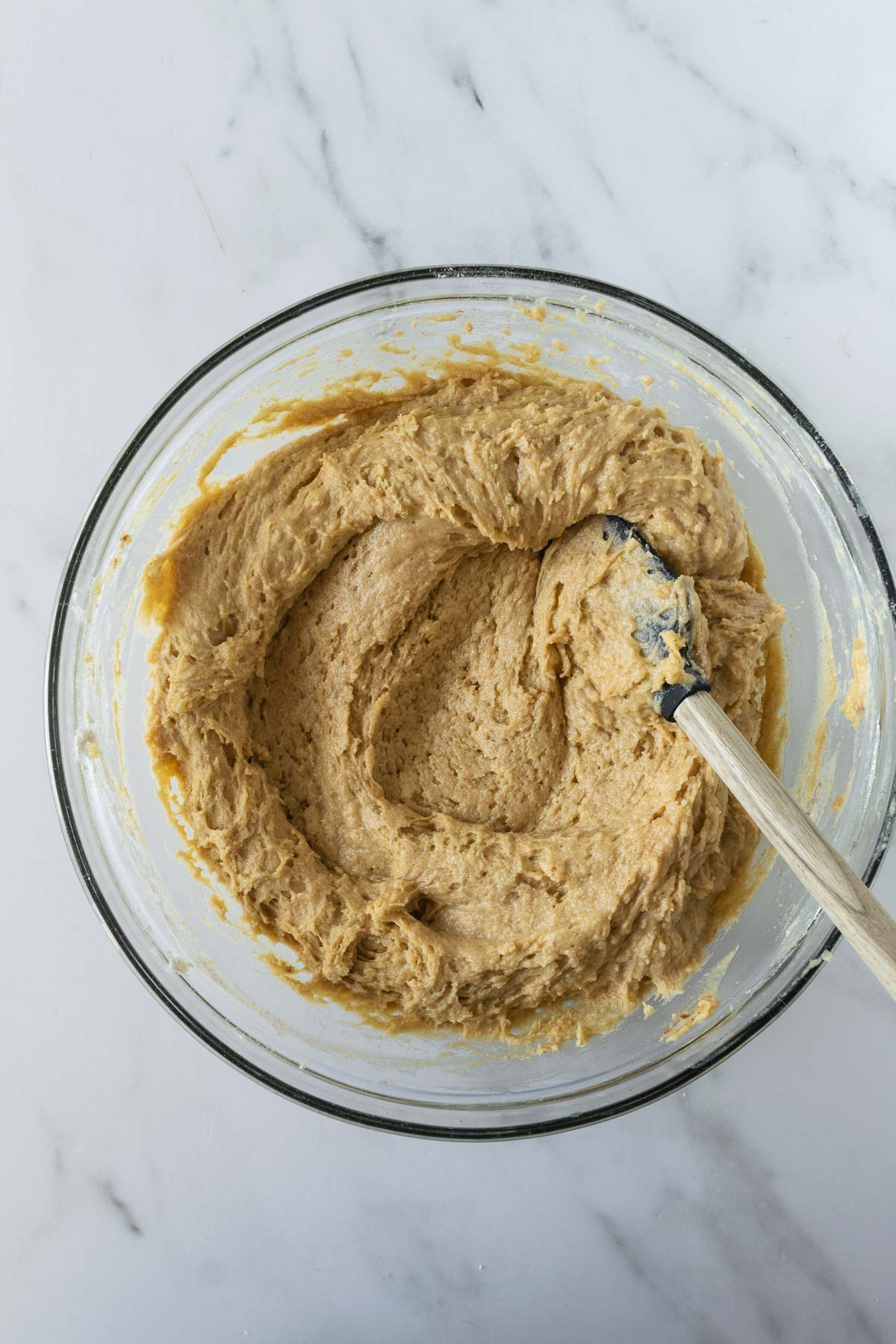 mixed apple cake batter with a spatula in a glass bowl on a white table.