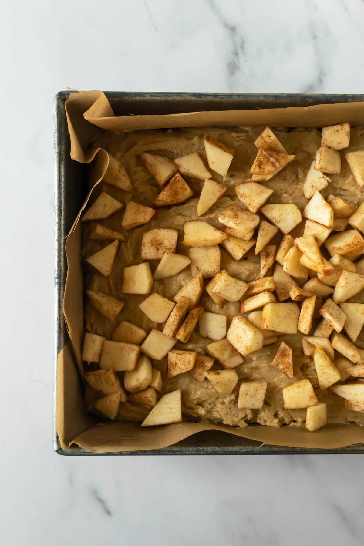 apple cake batter with chopped cinnamon apples on top in a baking dish.