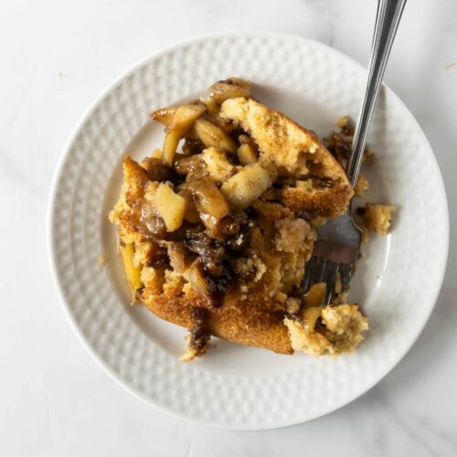 baked apple cinnamon pancakes with cooked apples on a white plate with a fork.