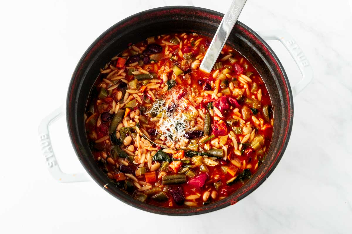 minestrone soup in a black pot with a silver ladle.