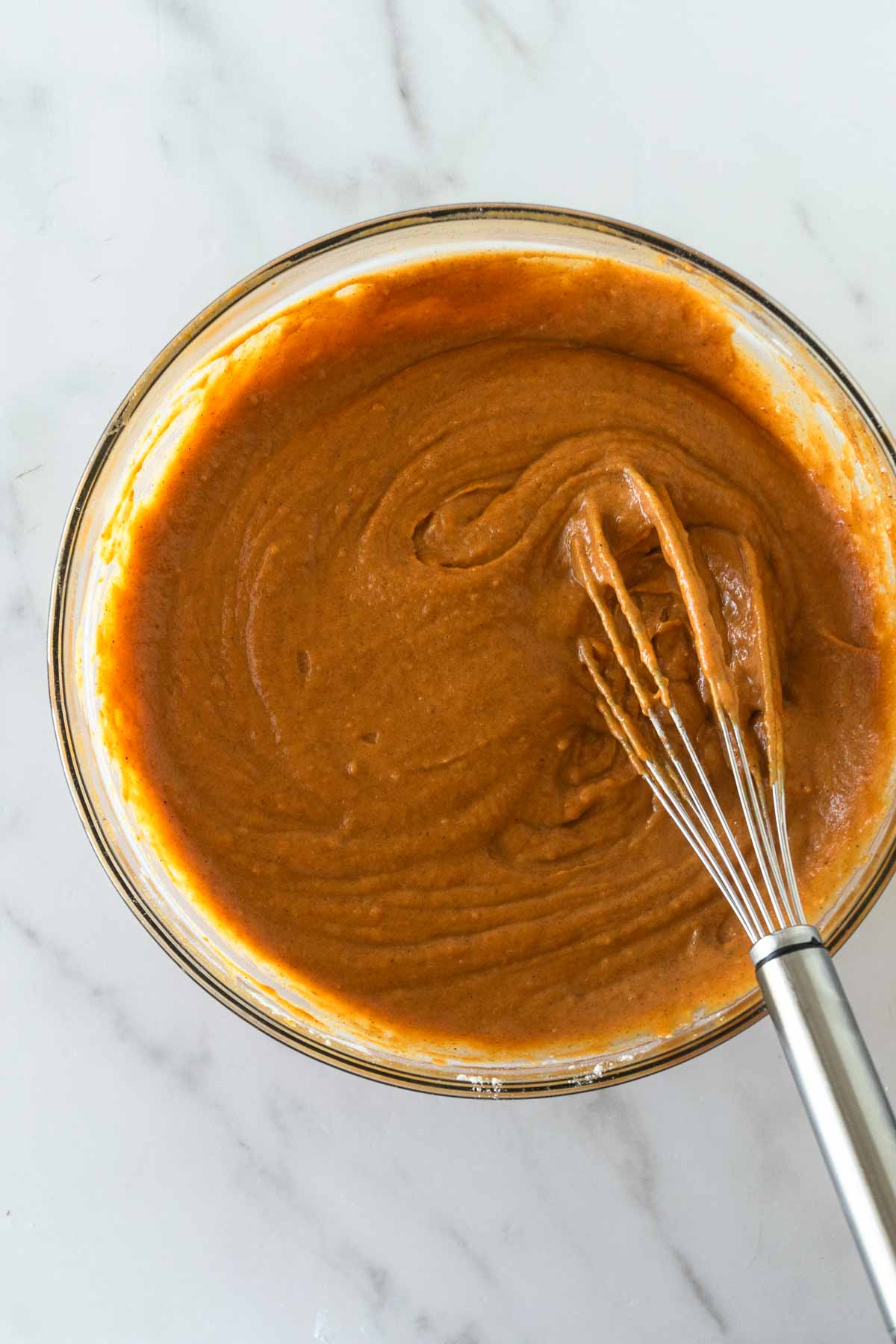 whisked pumpkin bread batter with a whisk in a bowl on a white table.