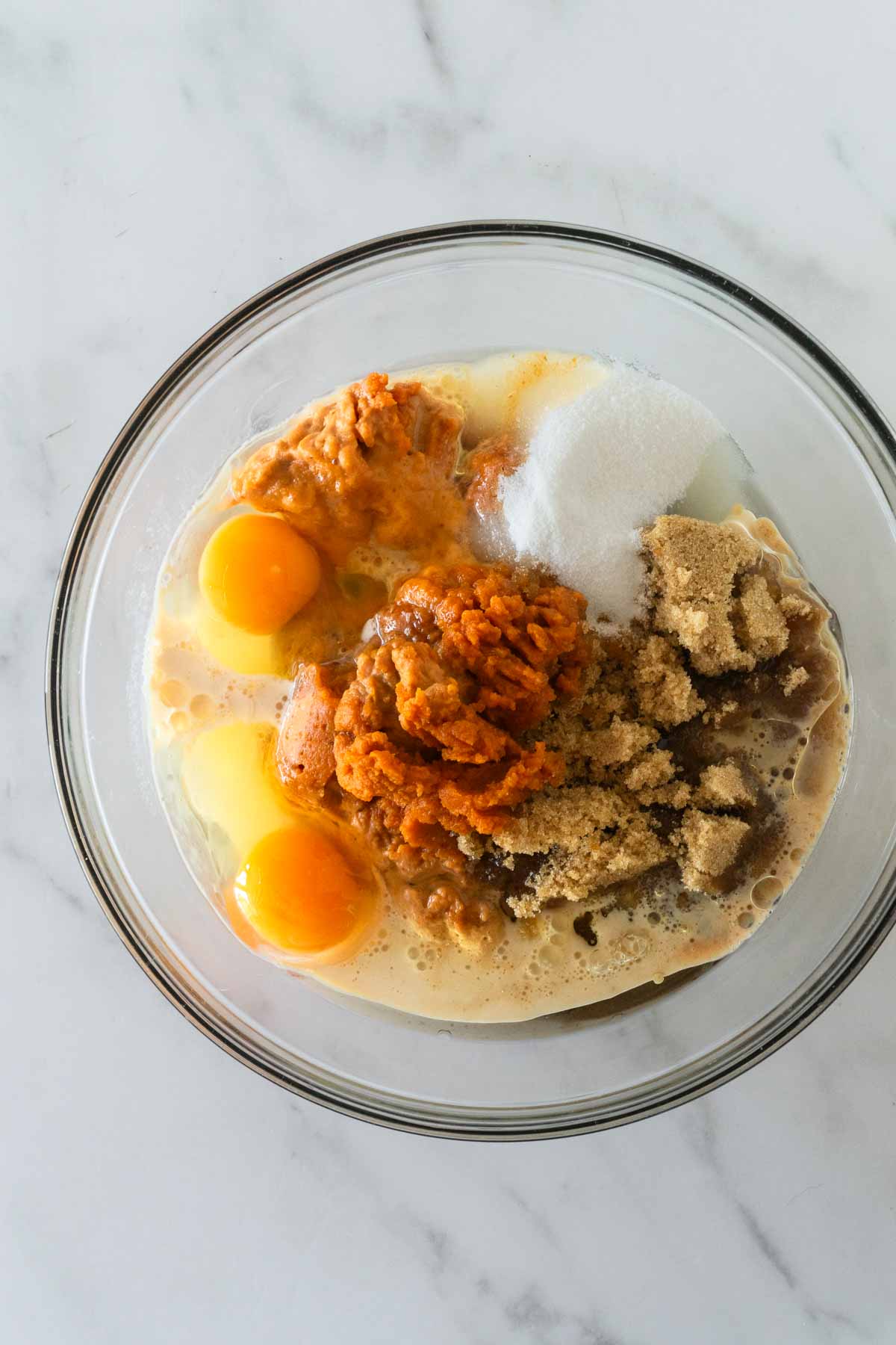 wet ingredients for pumpkin bread in a glass bowl on a white table.