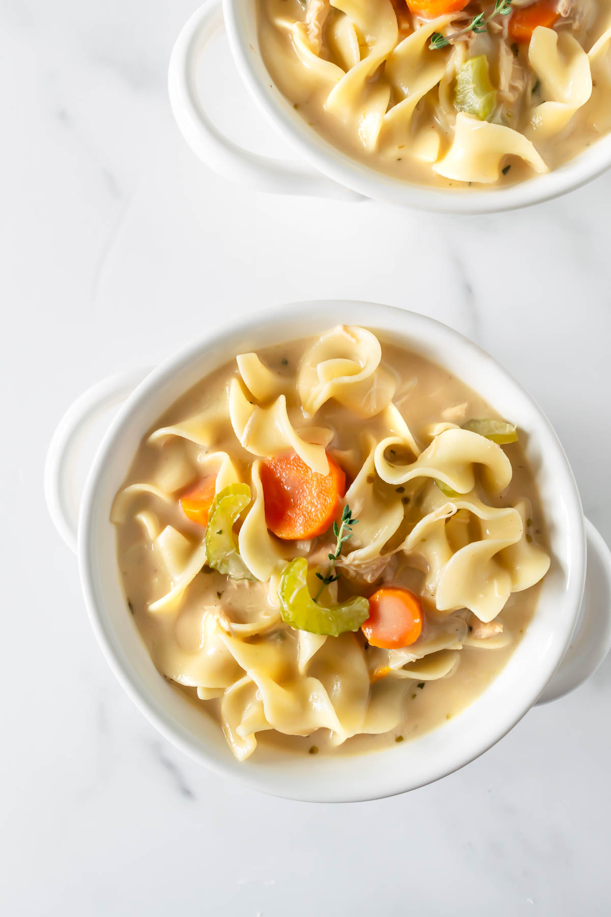 homemade creamy chicken noodle soup in a bowl on a white table.