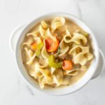 homemade creamy chicken noodle soup in a white bowl.