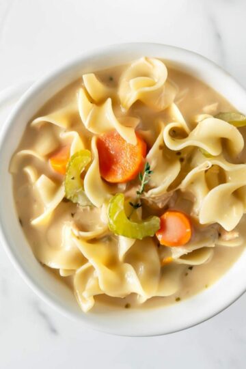 homemade creamy chicken noodle soup in a white bowl.