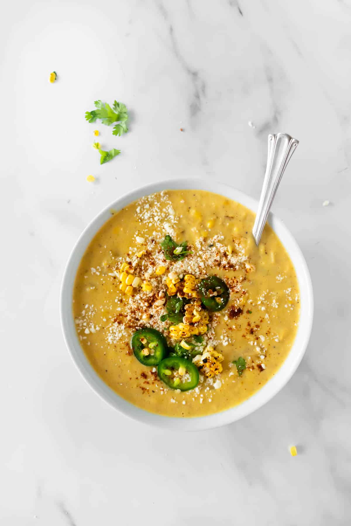 corn chowder in a white bowl topped with jalapeños, corn, and cheese with a spoon.