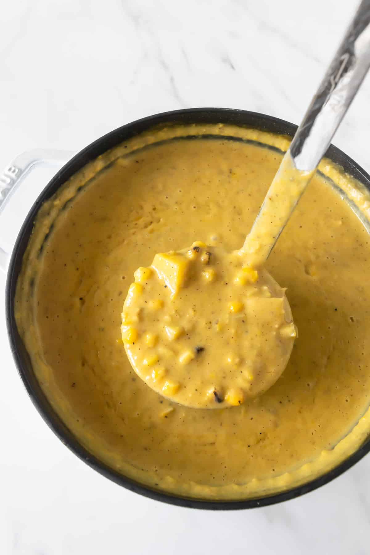 corn chowder a black pot on a white table with a ladle.