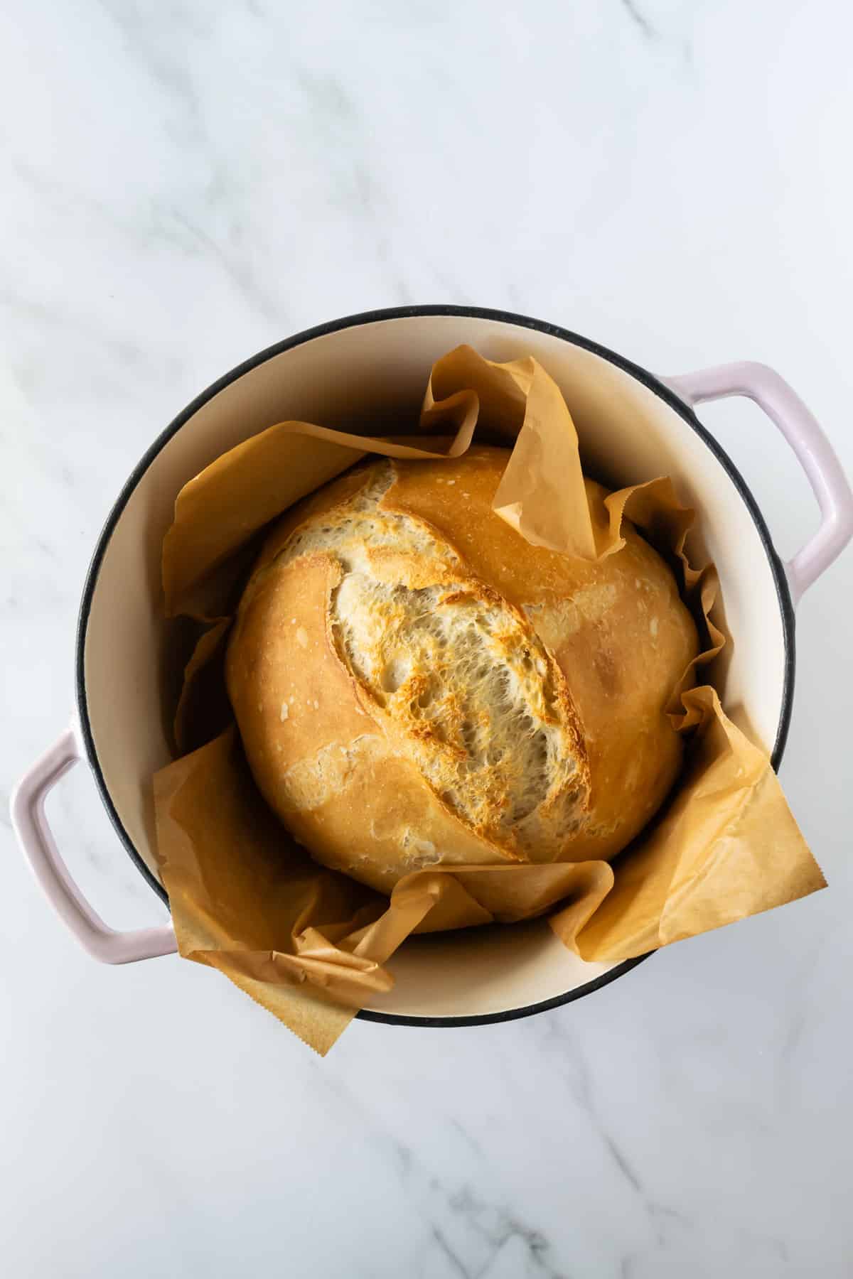 loaf of no knead bread in a pink dutch oven.