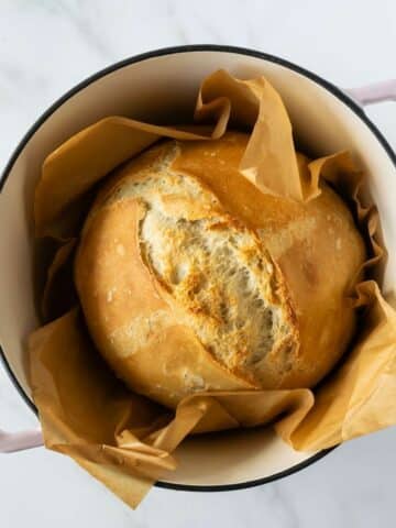 loaf of no knead bread in a pink dutch oven with parchment paper.