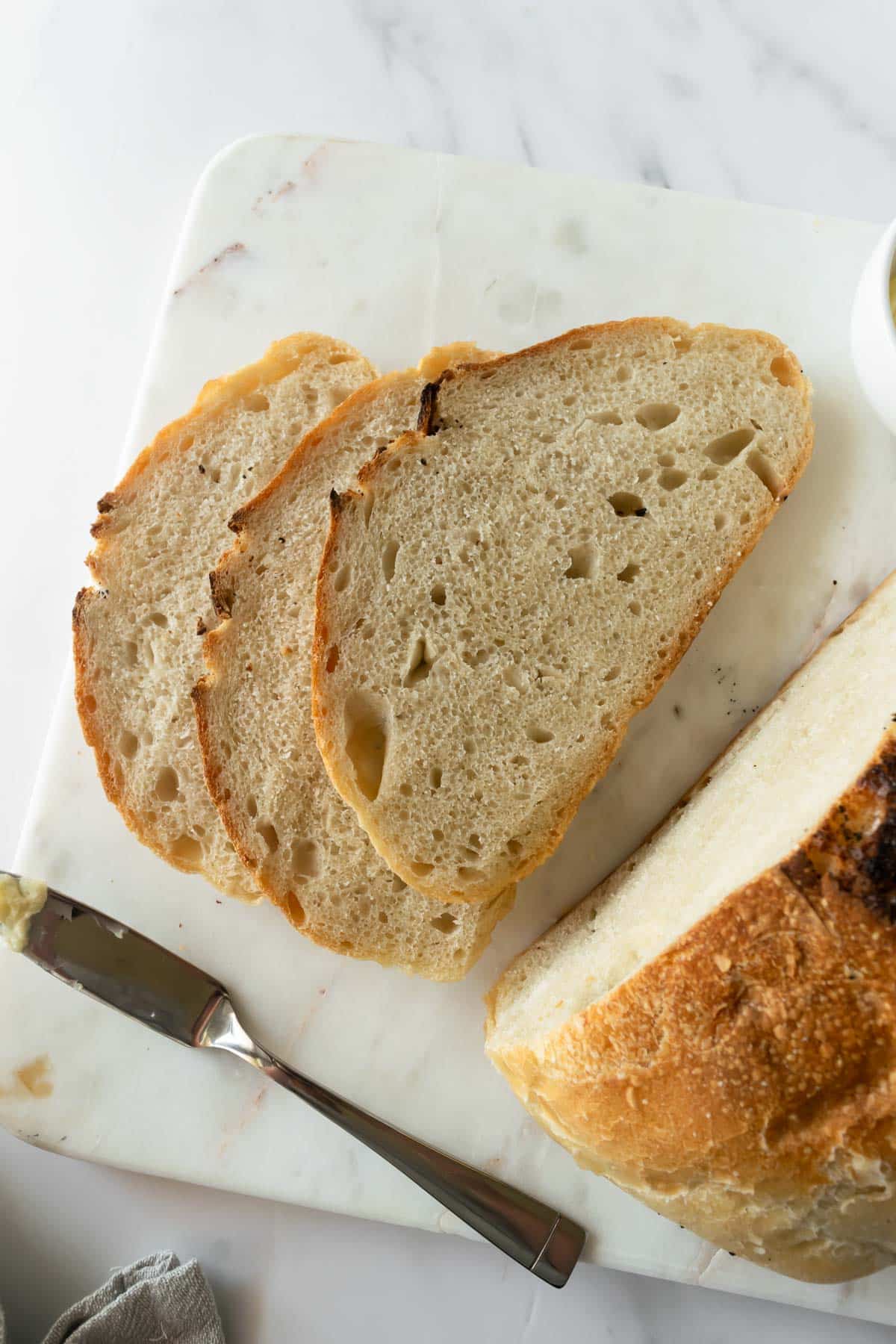 slices of no knead bread on a marble cutting board with a butter knife.