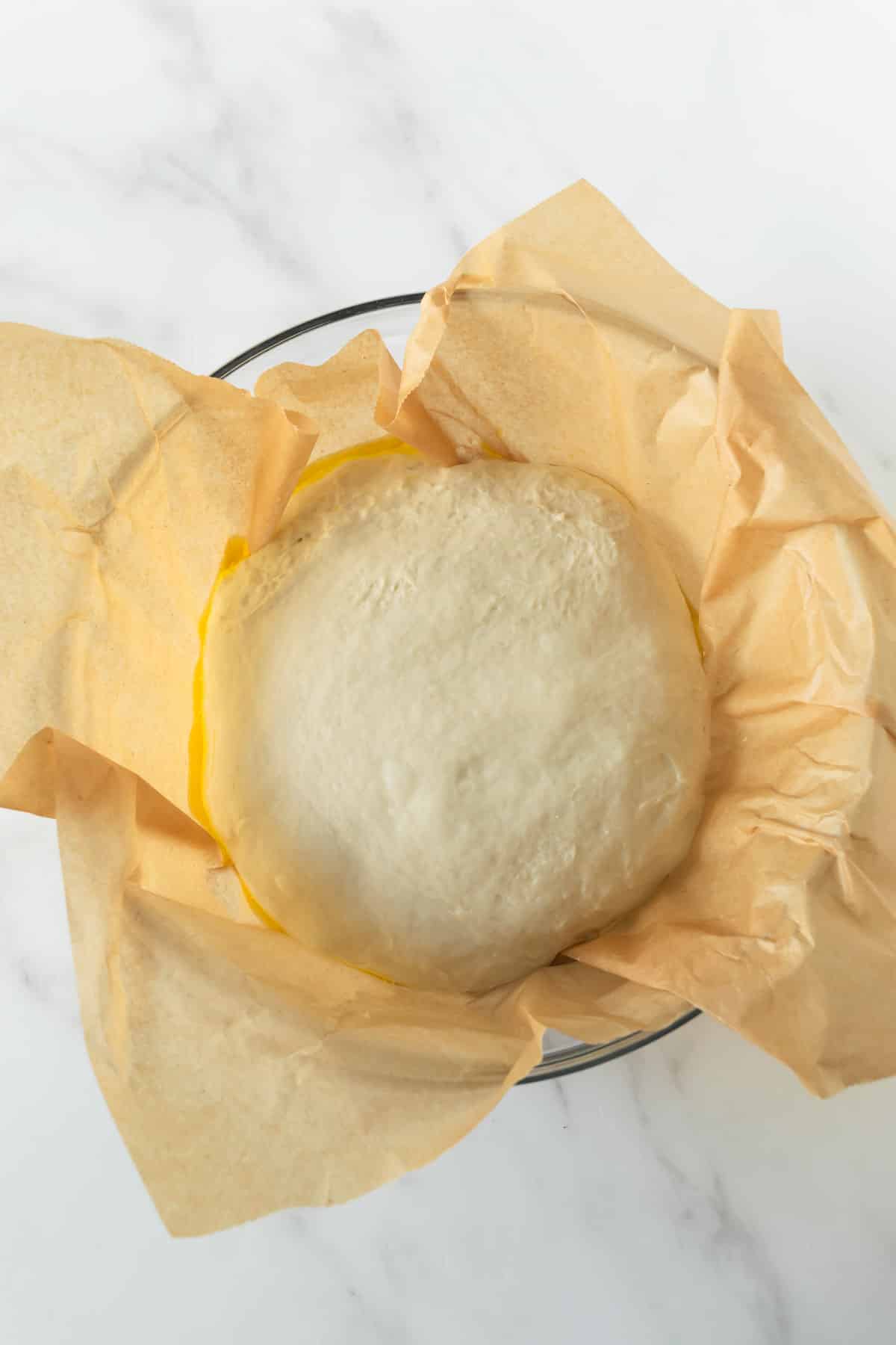 bread dough resting in a glass mixing bowl with parchment paper.