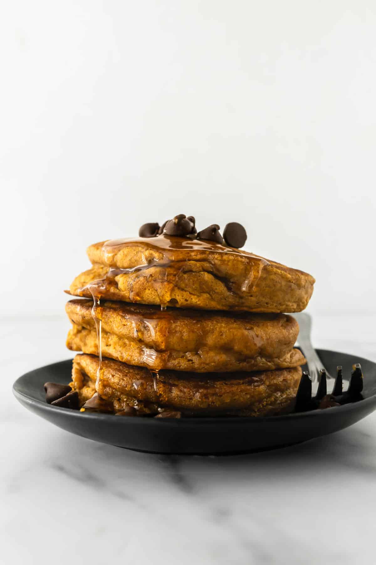 three pumpkin pancakes stacked on a plate with a fork.