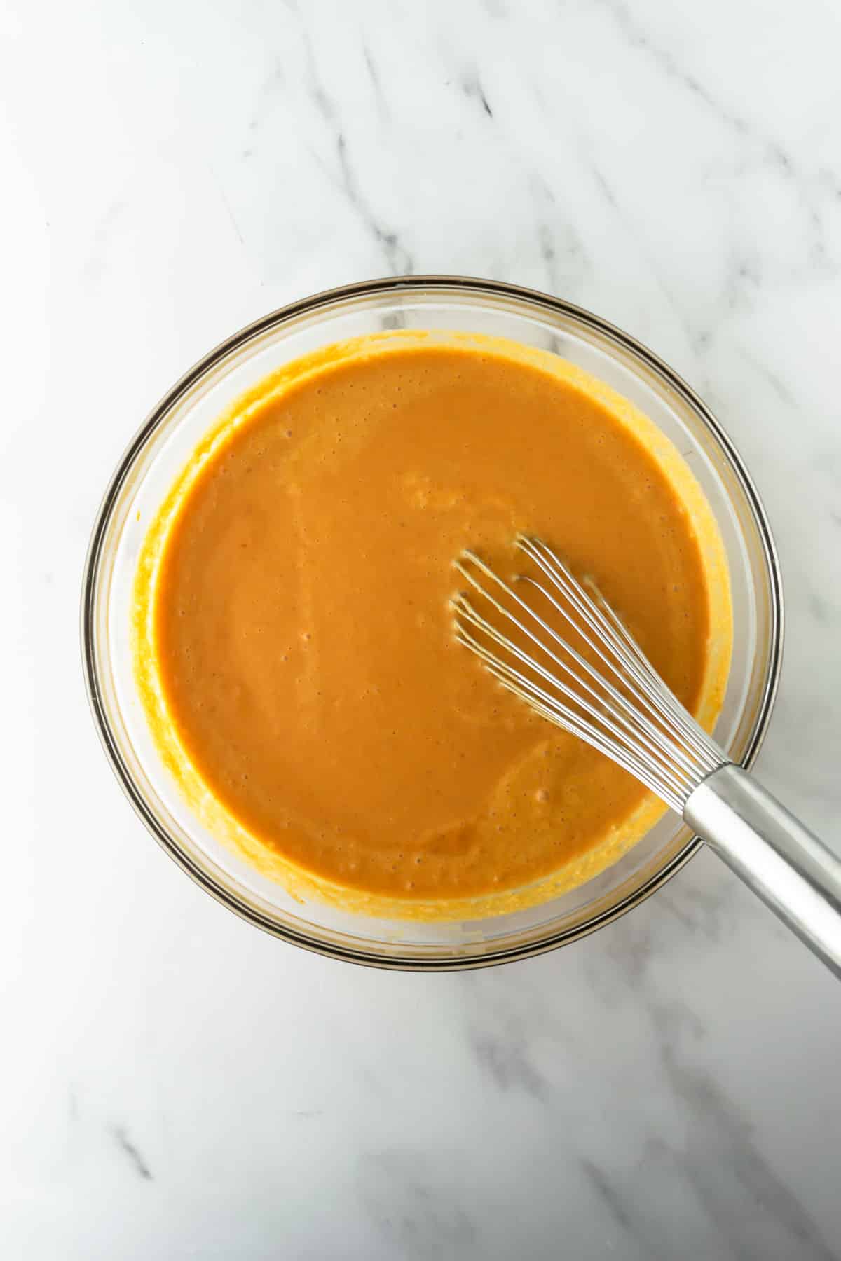 pumpkin pancake batter in a glass bowl with a whisk.