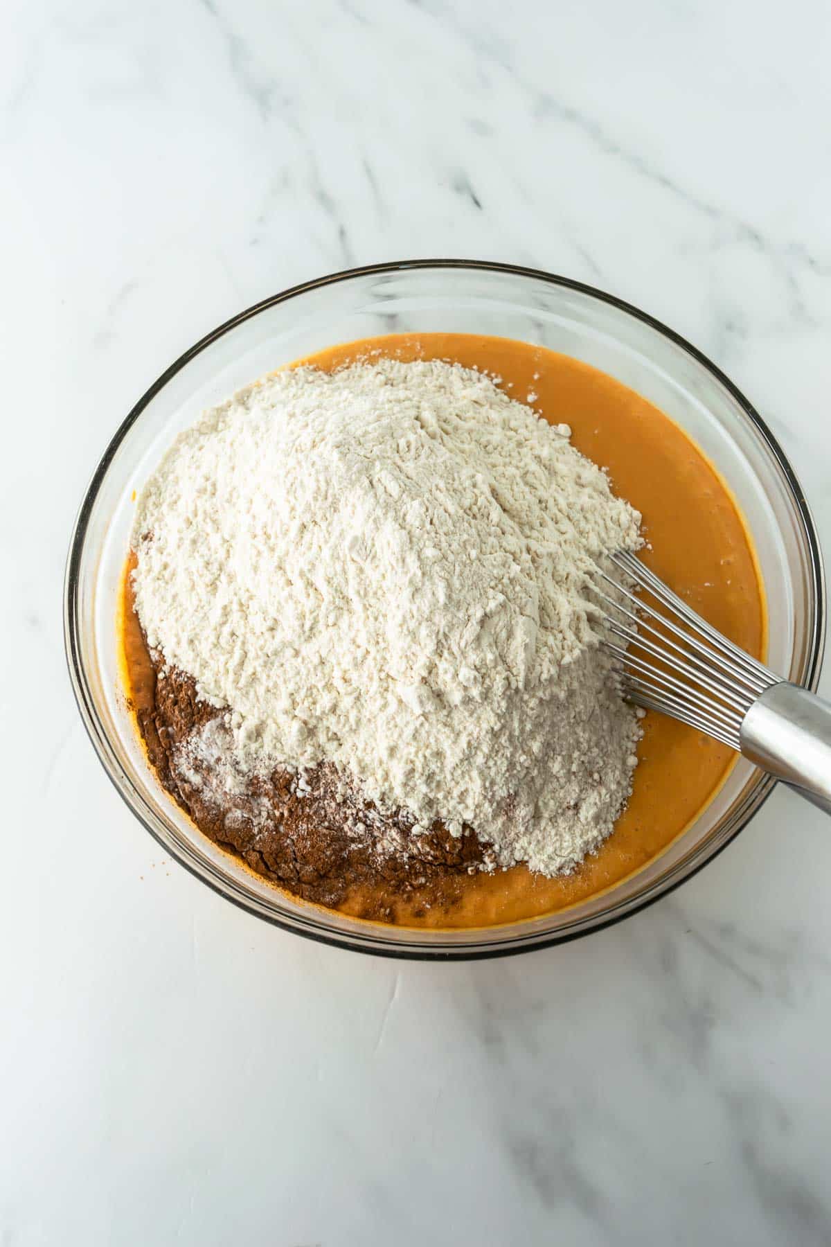 flour and cinnamon on top of pancake batter in a glass bowl with a whisk.