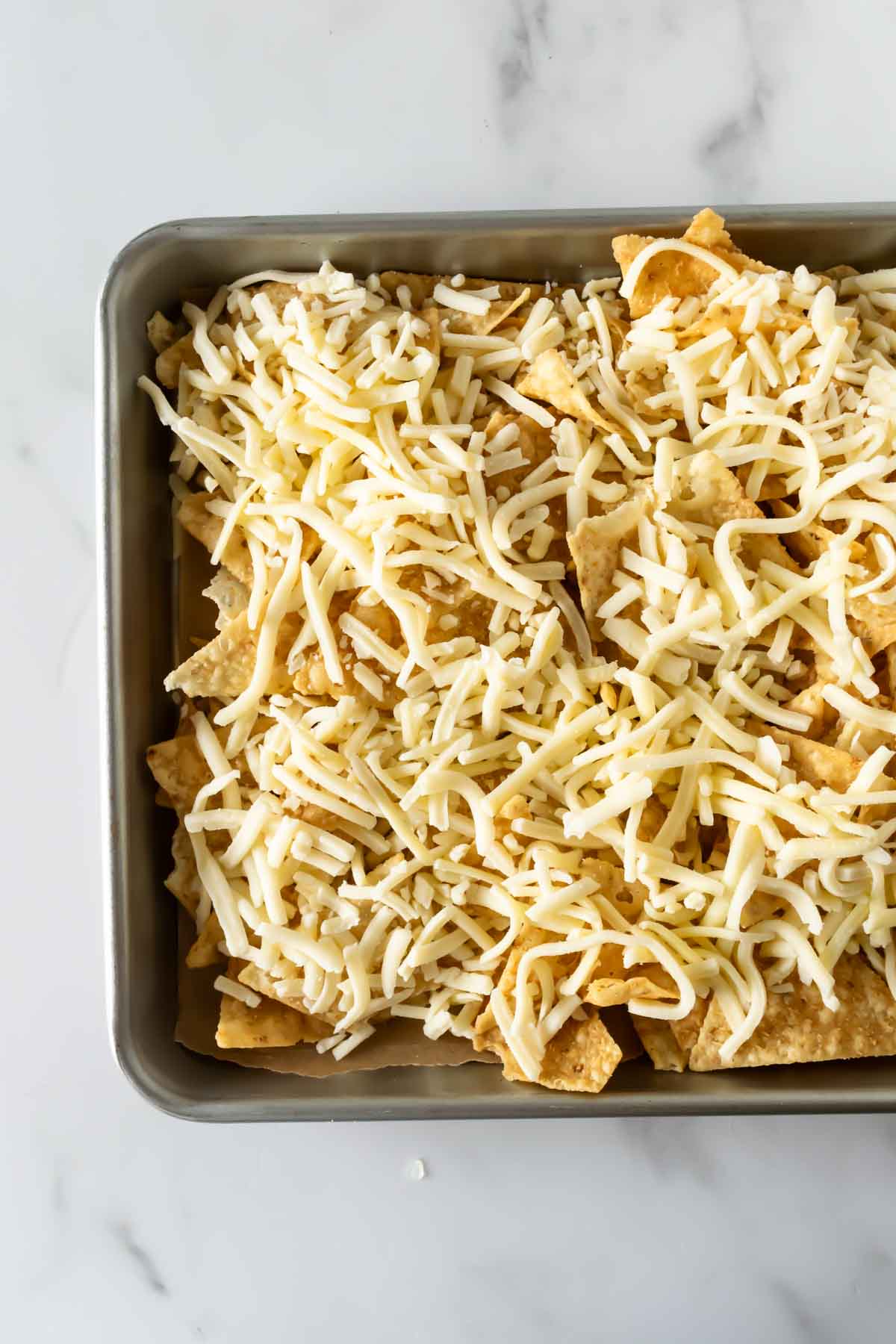 tortilla chips on a baking sheet topped with shredded cheese.