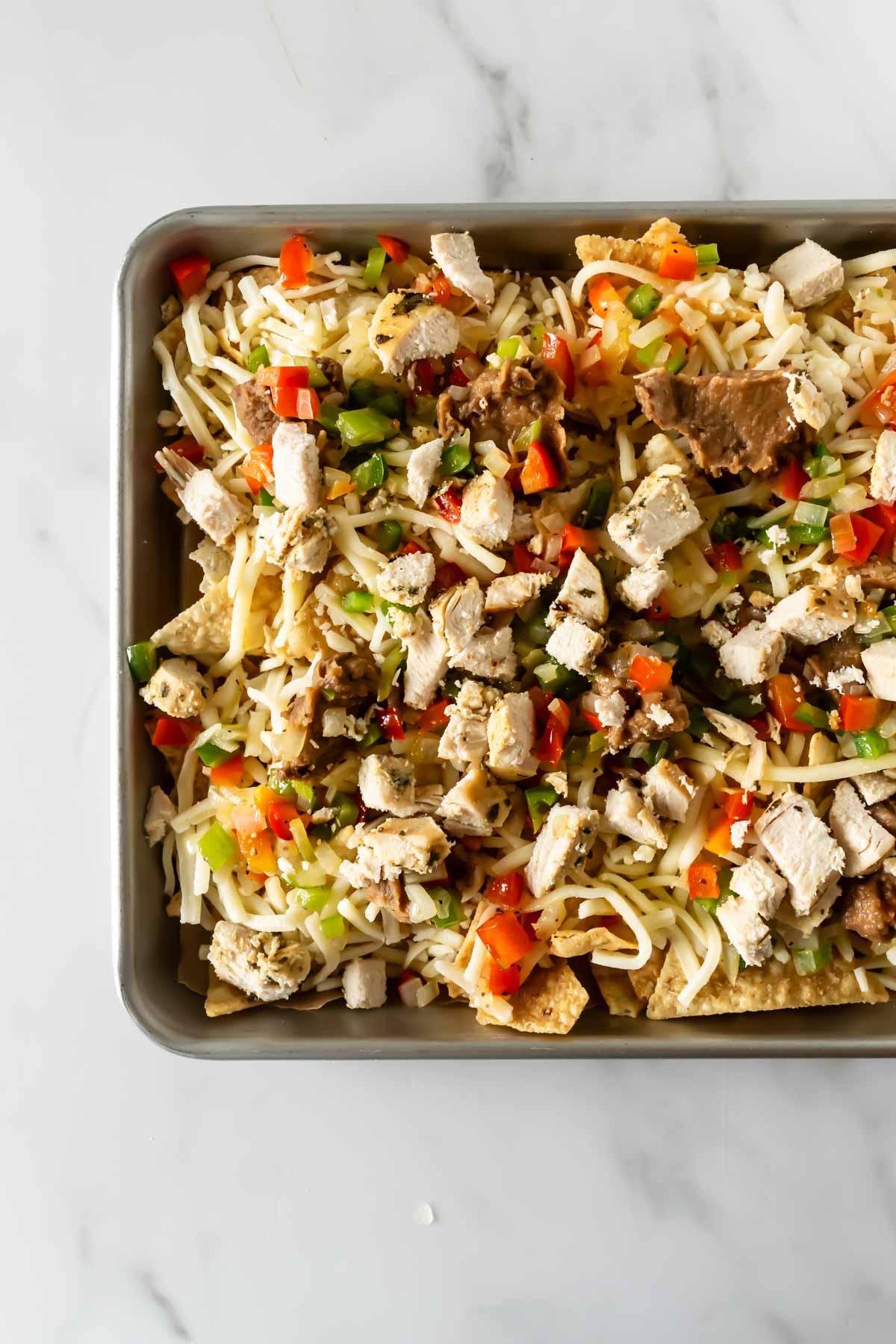 tortilla chips on a baking sheet topped with toppings and shredded cheese.