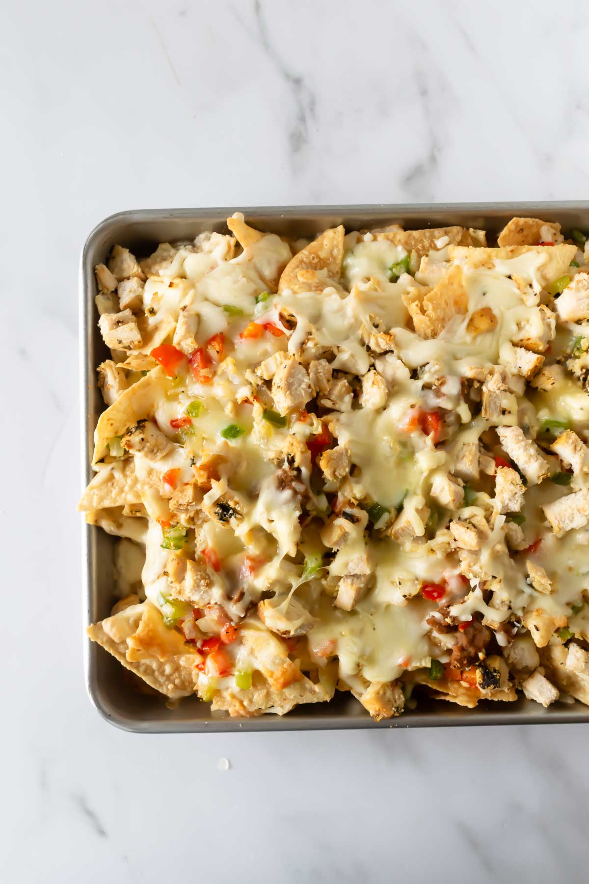 tortilla chips on a baking sheet topped with melted shredded cheese and toppings.