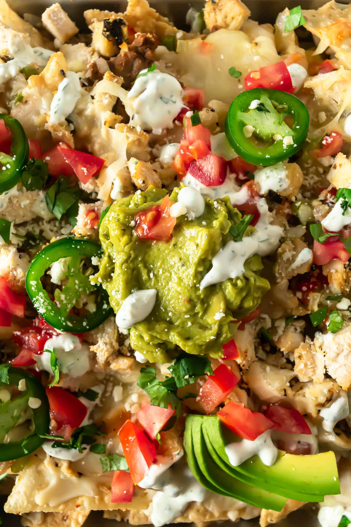 close up of loaded sheet pan nachos with toppings like guacamole, sour cream, tomatoes, and sour cream.